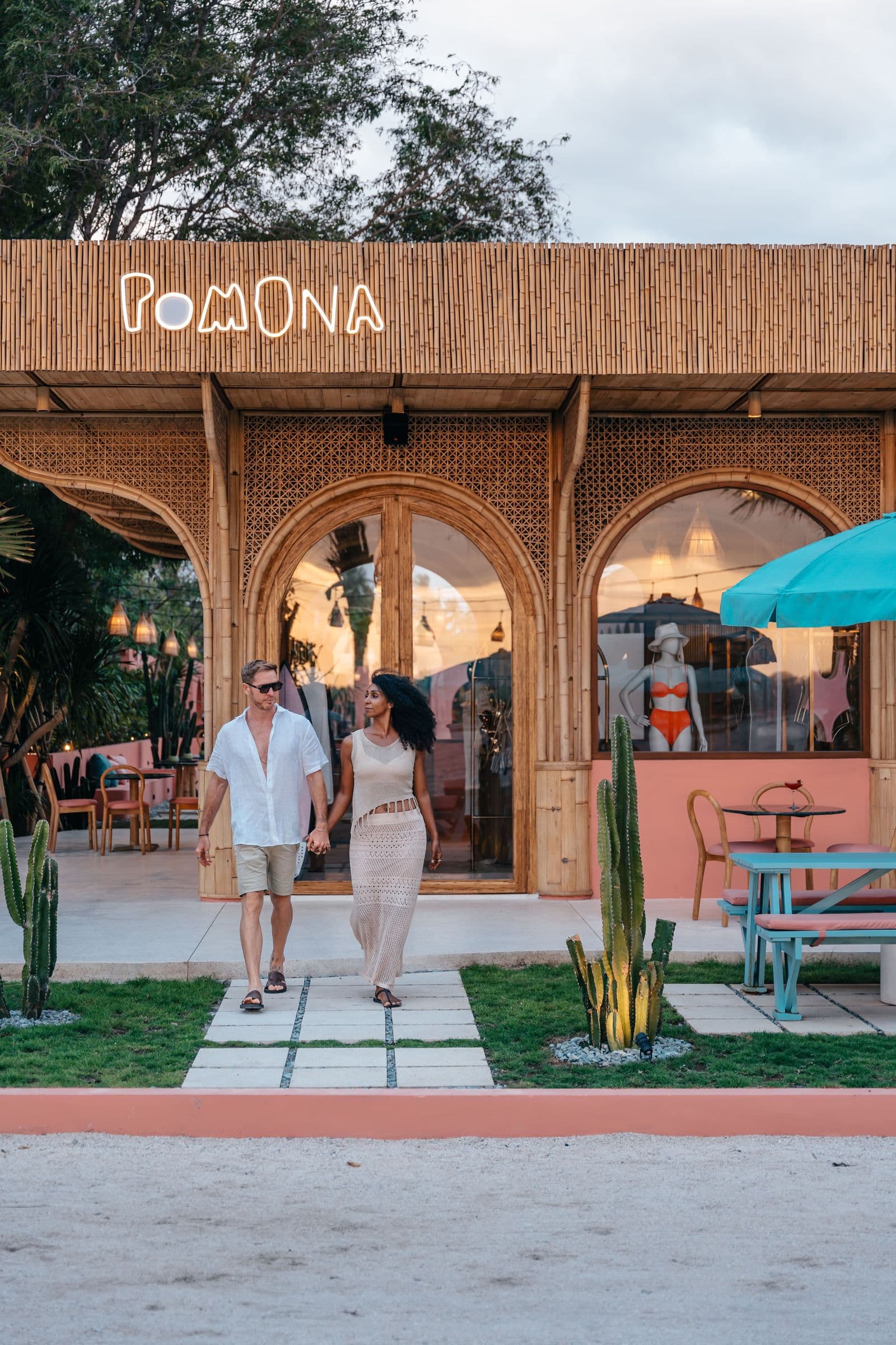 A couple walking out of Pomona at dusk, the sign lit behind them